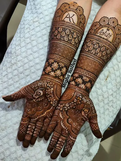 The bride's name 'Ashiti' and the couple's initial 'AK' are featured prominently on the arms in this personalized bridal design, surrounded by lotus bands and peacock motifs.