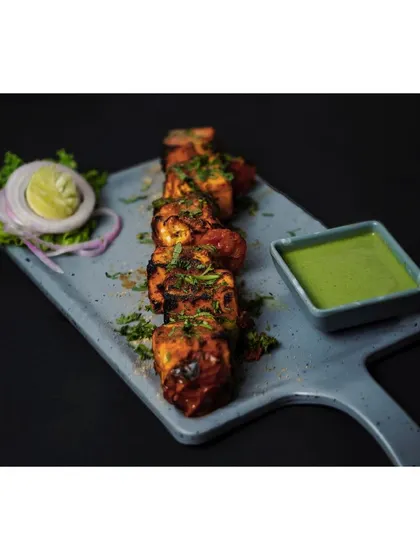 Grilled paneer tikka presented on a long platter with green chutney and a side salad. The image is shot against a solid black background to emphasize the food, a technique perfect for menus and ads.