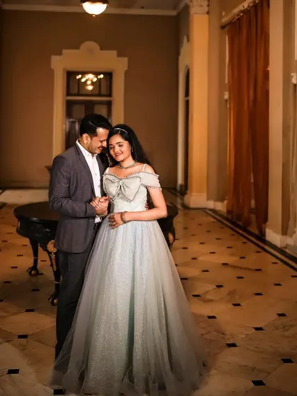 A classic pose from a pre-wedding shoot in a heritage location. The soft blue of her off-shoulder gown complements his grey suit, creating a sophisticated and timeless look.