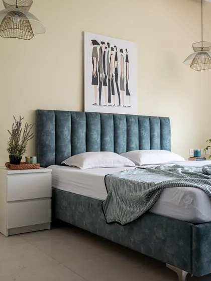 A simple yet sophisticated bedroom featuring a channel-tufted headboard in a calming blue fabric. The look is completed with minimalist white nightstands and woven pendant lights that add a touch of warmth.