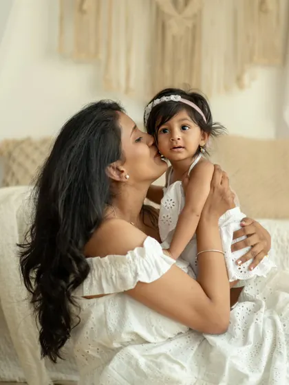 A mother gives her daughter a gentle kiss on the cheek. The daughter's sweet, calm expression makes this a very tender and loving portrait.
