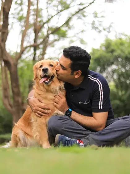 A joyful moment between a man and his Golden Retriever, sharing a kiss in a sun-drenched park, capturing pure affection.