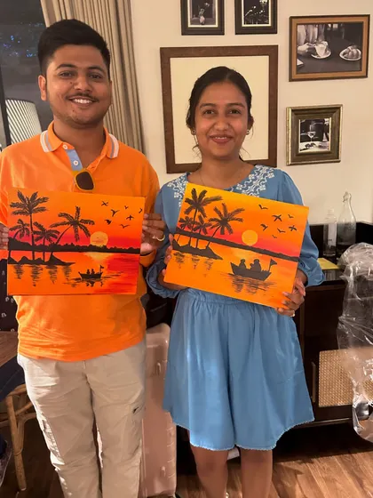 A happy couple posing with their matching sunset silhouette paintings.