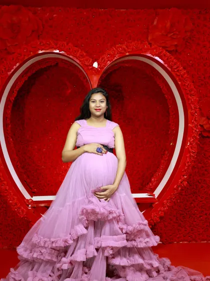 A solo maternity portrait in a lovely lavender ruffled gown, taken against a vibrant red heart-shaped backdrop in our studio.