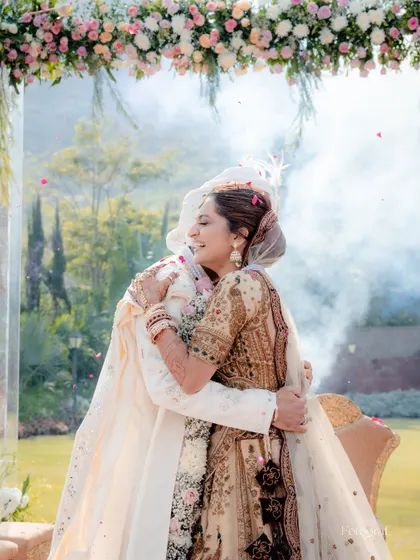 A hug that says everything. This emotional embrace under the floral mandap captures the profound connection between the couple right after their vows.