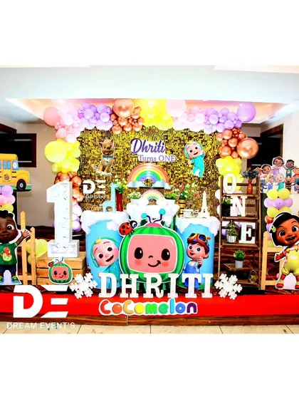 A dazzling Cocomelon first birthday for Dhriti. The setup includes a gold sequin backdrop, character cutouts, and a large 'ONE' sign, blending the fun of the cartoon with a touch of glamour.