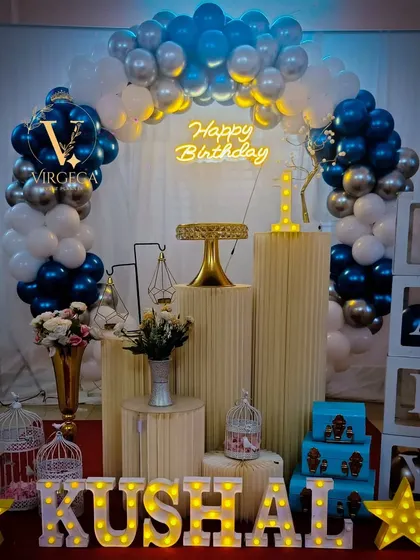 A classic blue, silver, and white first birthday setup with a balloon arch, 'BABY' blocks, and marquee letters.