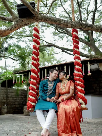 A cross-cultural couple enjoys a moment on the swing, decorated with red and white flowers, a vibrant and happy scene.