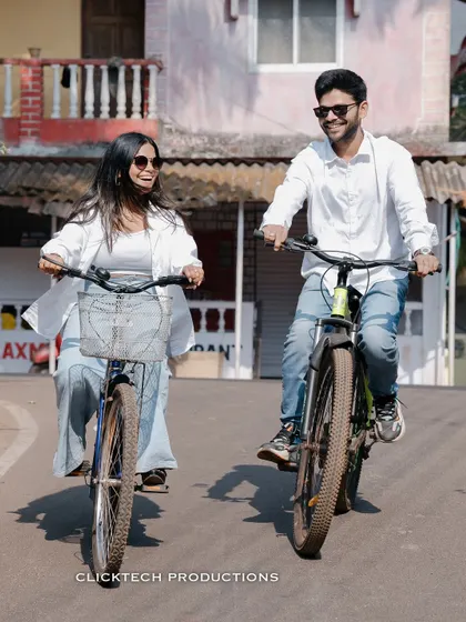 A joyful, candid shot of a couple riding bicycles through a Goan village, capturing their laughter and the local atmosphere.