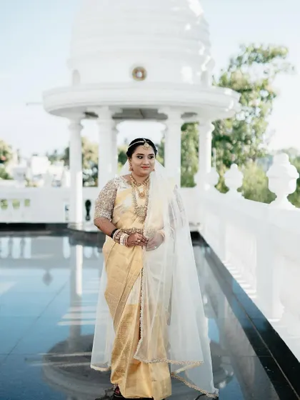 A full-length shot of a bride in a magnificent golden saree with a custom embroidered veil.
