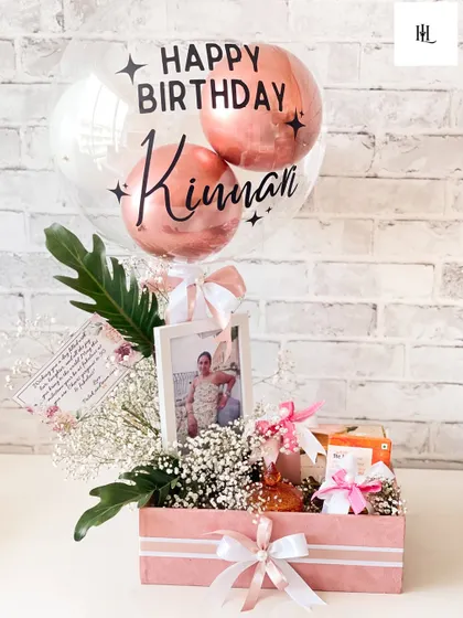 A birthday hamper should feel personal and full of joy. This one, designed in shades of pink, includes a custom photo frame, a personalized balloon for Kinman, and a curated selection of her favorite things, all nestled in a bed of baby's breath.