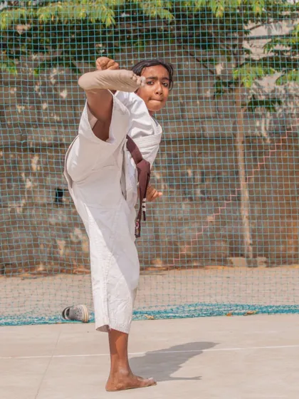 A young student with a brown belt executing a high kick with precision, showing that advanced skills are developed from an early age.