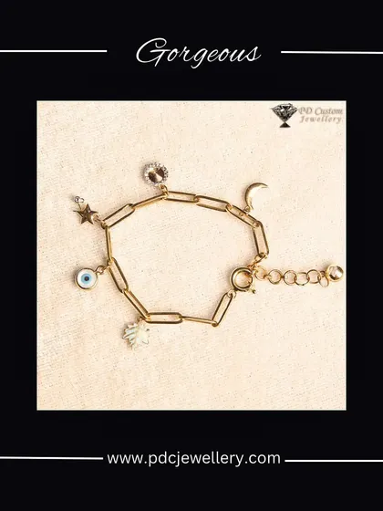 A gorgeous and trendy evil eye charm bracelet. This piece features a paperclip-style gold chain adorned with various diamond-studded charms like a star, moon, and hamsa hand.