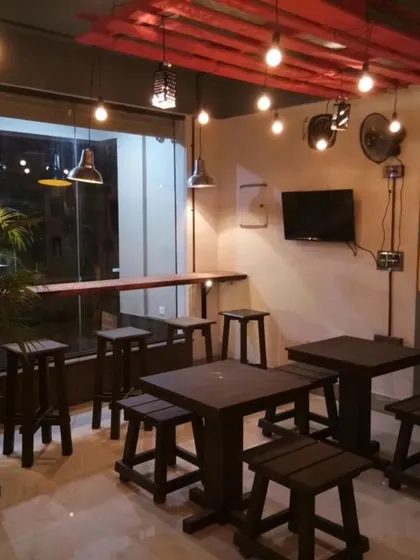 A cozy corner in a cafe we designed, featuring custom-built wooden tables and stools. The warm, industrial lighting and natural plant accents create a welcoming spot for customers.