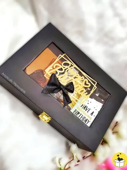 The closed view of a luxe hamper for men. The elegant black box with a clear window and a beautiful bow promises something special is waiting inside.