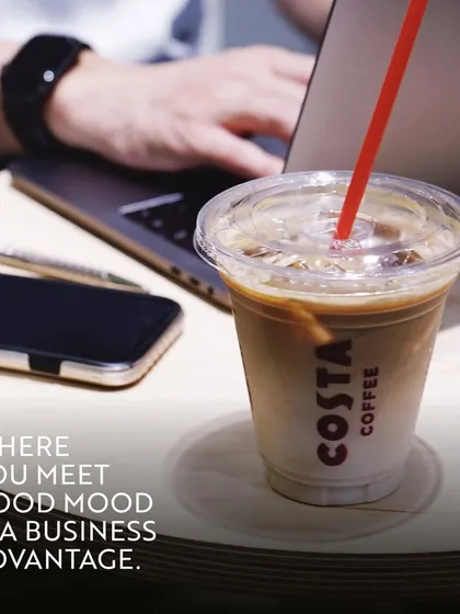 An iced coffee from Costa sits next to a laptop and phone. This image perfectly illustrates that a good mood is a business advantage, and the right setting can make all the difference.