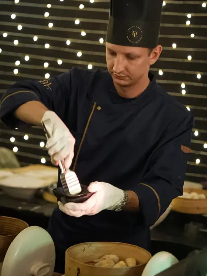 Our international chefs bring authentic skills to your event. Here, a chef carefully prepares a serving of freshly steamed dim sum, ensuring each piece is presented perfectly.