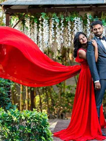 A stylish pose in a garden with a gazebo, the bride's red trail gown spread out, showcasing a blend of nature and high-fashion photography.