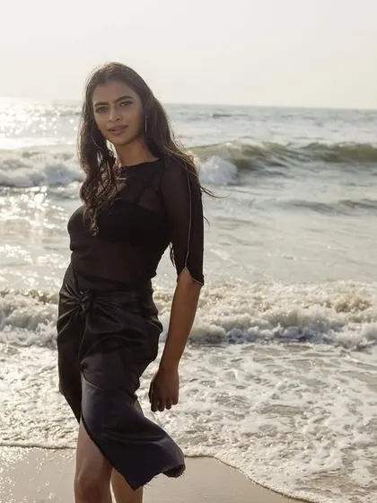 A portrait from the 'TIDE' series, shot on the beach at sunset. The styling is simple and raw, with a sheer black top and skirt that interact with the water and light to create a natural, elemental feel.