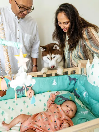 A loving family scene where parents and their husky look into the crib at their newborn baby.