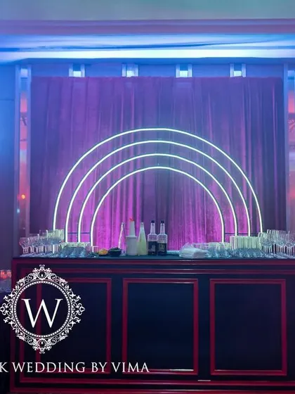 A bold and luxurious reception with a red and black color scheme. The decor includes rich red roses, modern crystal candelabras, and a stylish bar with a neon arch backdrop.