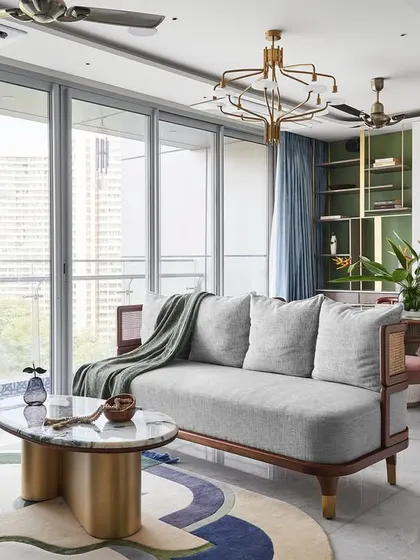 The living room is filled with natural light from the expansive windows. The custom 'Ananta' center table with its infinity-shaped brass base and the colorful rug from The Hatsu anchor the seating area.