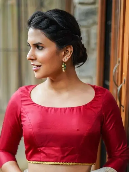 A model wears a simple red blouse with elegant green and pearl drop earrings.