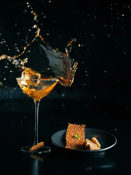 A dynamic shot of 'The Wisdom' cocktail, capturing the splash of pine needle whisky as it hits the ice. This drink is a blend of whisky, prekese bark, and dry vermouth.