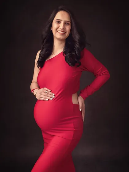 A smiling and confident portrait in a striking red one-shoulder gown. The dark background makes the color and her glow stand out.