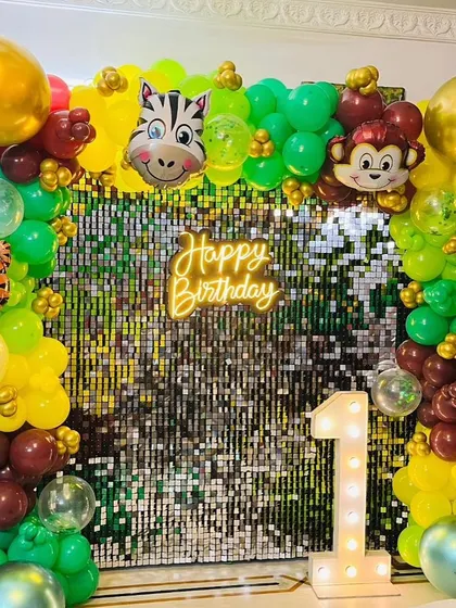 A close-up of the jungle-themed birthday backdrop, showing the 'Happy Birthday' neon sign and the light-up number '1' against the sparkly sequin wall.