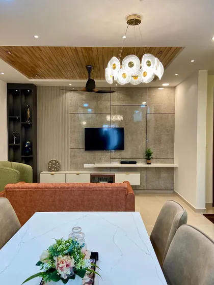 A view from the dining area into the living room, showing the cohesive design language. The wooden ceiling panel and textured walls in the living room complement the elegant dining setup.