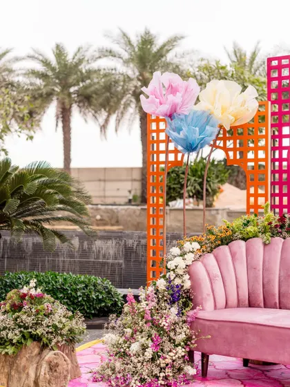 A pink scalloped sofa surrounded by flowers, with oversized paper flowers and colorful lattice screens in the background.