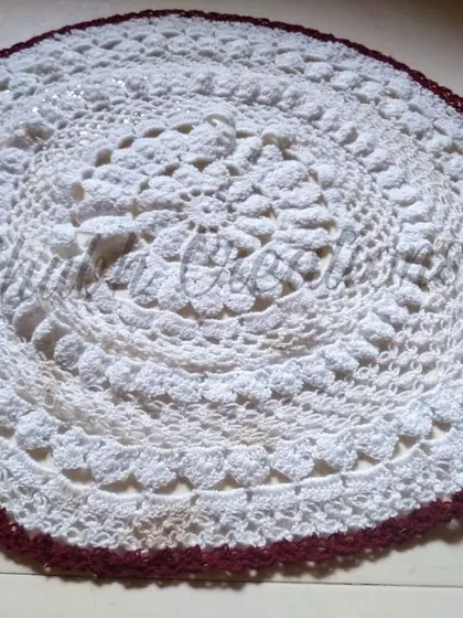 A full view of the large white and maroon crochet doily, perfect as a centerpiece for a large table.