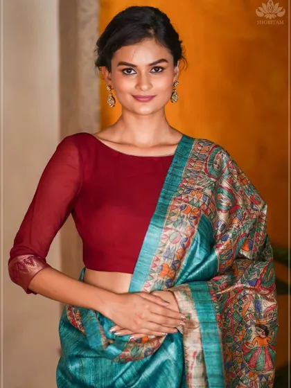 Here, a model wears a stunning turquoise tussar silk saree with Madhubani and Kalamkari inspired prints. It is paired with a simple red blouse to highlight the saree's intricate artwork.