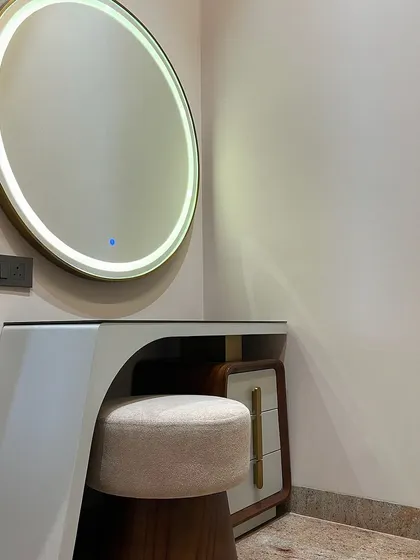 We designed a unique, modern dressing table for this room. The asymmetrical design combines a wood-finish base with a sleek white top and a large, round backlit mirror.