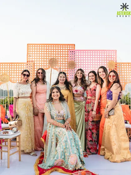 The bride with her bridesmaids at a vibrant outdoor Mehendi. The colorful geometric backdrop and bright floral decor created the perfect setting for fun group photos.