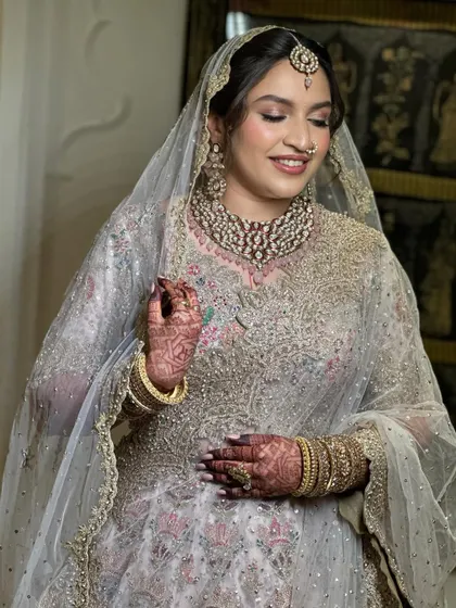 A lovely bride smiling, with her hair styled in a soft, low updo beneath a delicate net veil. This look is perfect for a Nikah or reception, offering a touch of modern elegance.