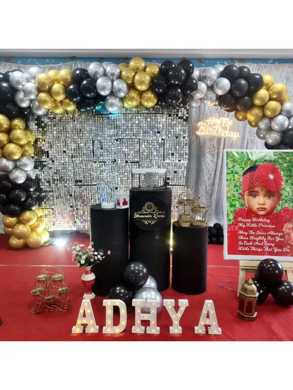 A glamorous birthday setup with a black, gold, and silver balloon arch over a shimmer wall.