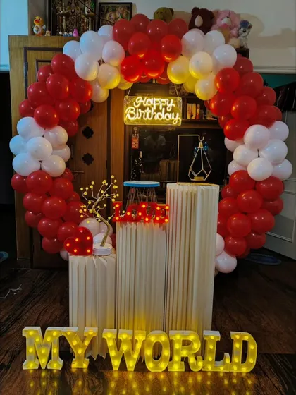 A classic romantic birthday setup in red and white. The circular balloon arch, light-up letters spelling 'Mine' or 'My World', and soft lighting make for a very personal and heartfelt surprise.