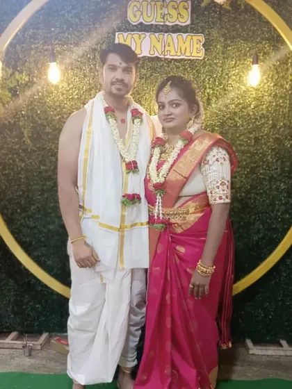 A couple poses in front of the circular naming ceremony backdrop. The combination of the green wall, floral decor, and warm lighting makes for great pictures.