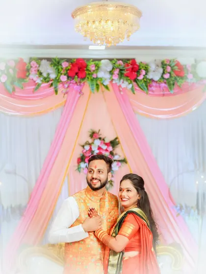 The couple holds hands, framed by a beautiful pink and white draped mandap. This soft, dreamy photograph captures the romance of their wedding day.