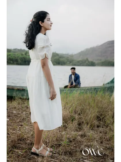 A beautiful solo portrait of the bride-to-be by the lake, with her partner visible in a boat in the background.