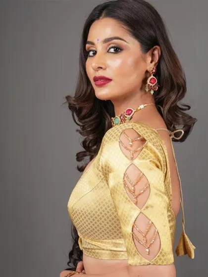 This model showcases a gold blouse with unique cutout sleeve details, paired with a multi-colored stone choker.