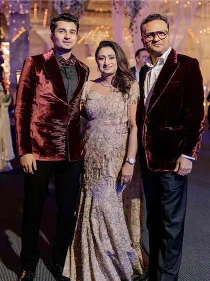 Creating unforgettable moments starts with impeccable style. For this cocktail soirée, we dressed the family in a coordinated palette of rich burgundy velvet and shimmering gold. The mother of the groom looks radiant in a Tarun Tahiliani gown, standing with her elegantly dressed husband and son.