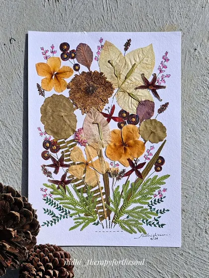 One of the pressed flower artworks styled with pinecones on a textured surface.