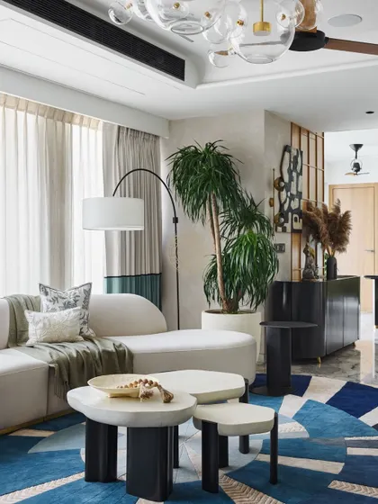 This living room in a Mumbai duplex blends Japandi style with natural materials. A large, geometric blue rug anchors the seating area, which features a curved white chaise and rounded coffee tables for a kid-friendly design.