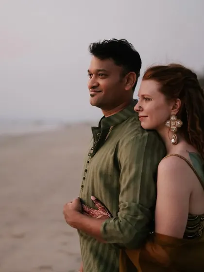 A serene portrait of the couple against the Goan coastline. Their tone-on-tone olive green and floral outfits blend beautifully with the natural, dusky setting of their sundowner event.