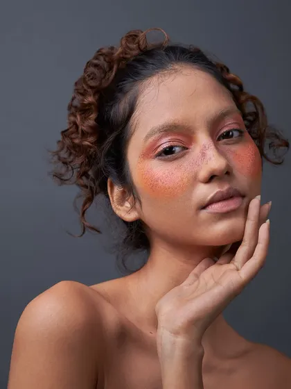 A close-up of an artistic makeup application. The wash of coral and pink blush over the cheeks and eyes creates a soft, watercolor effect that is both unique and beautiful.