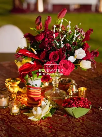 A vibrant centerpiece with red and white flowers on a table with a rich brocade cloth.