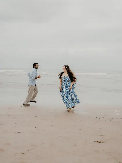 A wide shot of the couple running and laughing on the beach, capturing their free-spirited nature against the vast ocean backdrop.